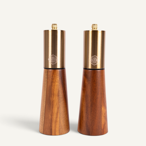 Two acacia wood salt and pepper mills with brushed brass tops, standing side by side on a light gray background.