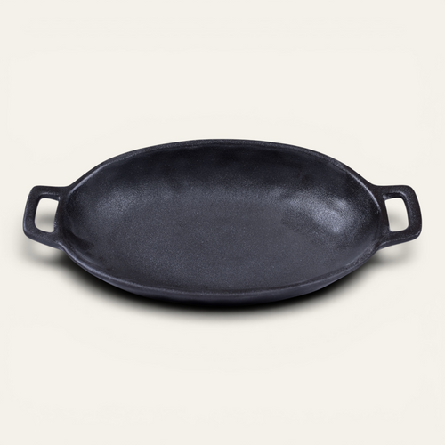 An oval black Japanese style ceramic serving bowl with two side handles, photographed on a light cream background.