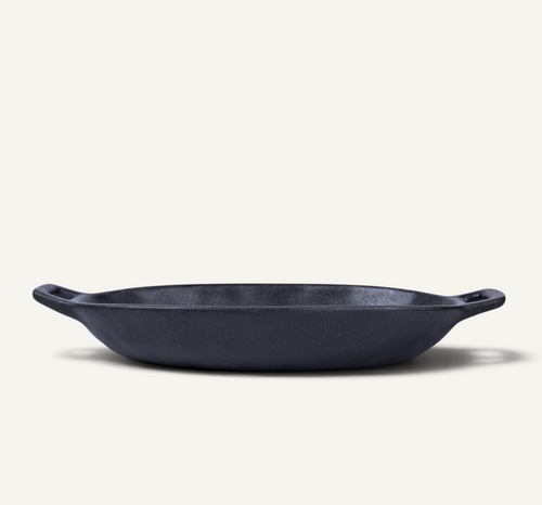 An oval black Japanese ceramic serving bowl with side handles, photographed on a clean, solid off-white background.
