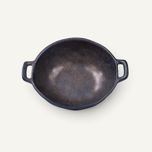 A Japanese style ceramic bowl with two side handles, photographed from a top-down perspective on a light cream background.