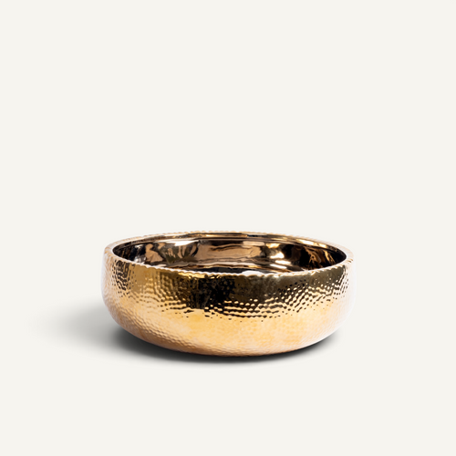 A small hammered ceramic bowl with a warm gold finish, photographed on a clean off-white background.