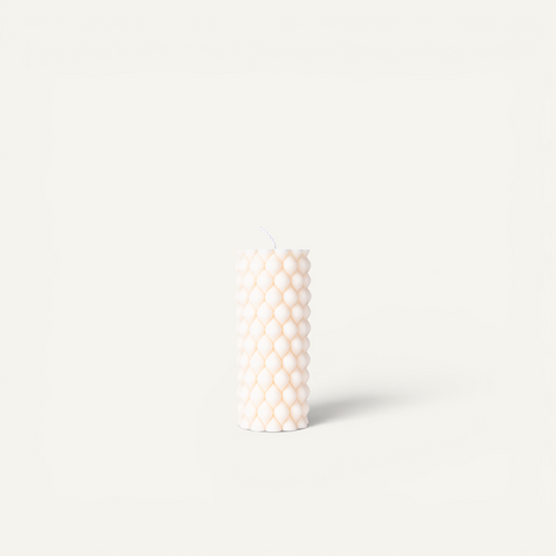 Three textured pillar candles standing upright in a row on a clean off-white background. The left candle is gray, the middle candle is terracotta, and the right candle is off-white.