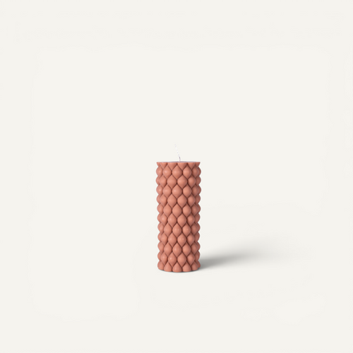 A textured, ribbed pillar candle in a muted terracotta color, standing upright against a clean, off-white background.