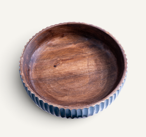 A round wooden bowl with a scalloped, fluted rim, featuring a dark brown wood interior and a glossy dark blue-gray exterior, shown on a light cream background.