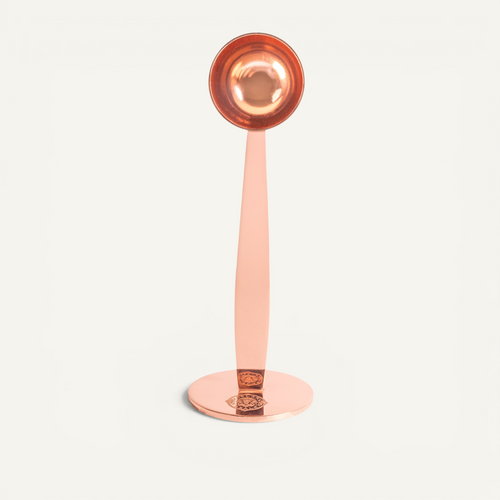 A stainless steel espresso scoop in rose gold color with integrated tamper, displayed on a white background.