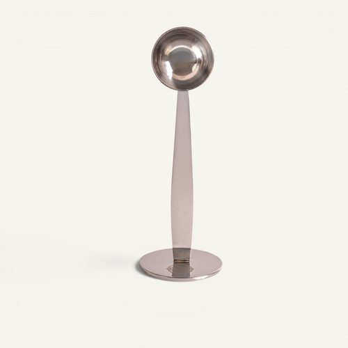 A stainless steel espresso scoop with integrated tamper, displayed on a white background.