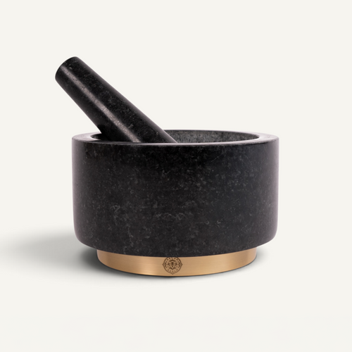 A black stone mortar and pestle set with a polished gold-toned circular base, photographed on a clean off-white background.
