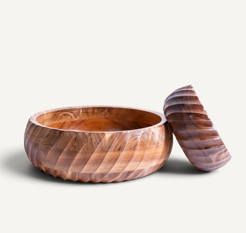 A round acacia bowl with a matching lid, both featuring a carved spiral pattern, displayed on a light beige background.