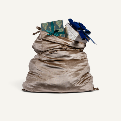 A large silk velvet Christmas sack in beige color filled with wrapped gifts, including a green patterned box with a teal bow and a silver box, isolated on a light cream background.