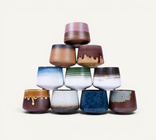 Stack of ceramic cups with various colors and patterns on a white background