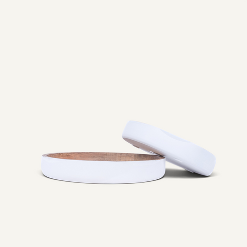 A minimalist white circular bowl with a wooden interior, shown with its matching lid propped behind it on a clean off-white background.