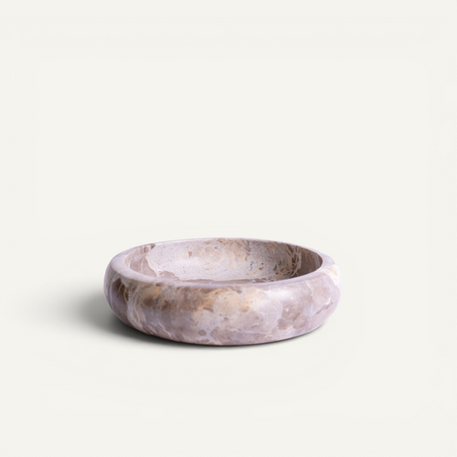A round stone bowl with a marbled lavender, beige, and brown pattern, photographed on a clean off-white background.