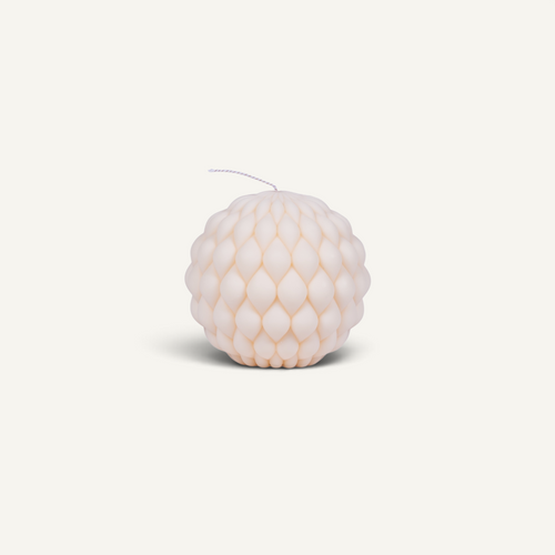 A single textured spherical candle in a pale blush pink color, featuring a dimpled, raspberry-like surface and a thin white wick, set against a solid off-white background.