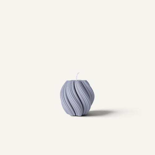 A ribbed, textured candle in a muted periwinkle or stone gray color, photographed against a solid off-white background.