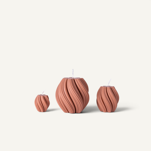 Three ribbed, vase-shaped candles in a terracotta pink color, arranged by size against a light off-white background.