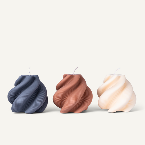 Three sculptural spiral-shaped candles in navy blue, terracotta, and cream, arranged side by side on a light beige background.
