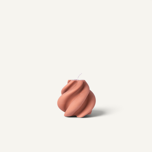 A sculptural, ribbed candle in a dusty terracotta color, featuring a twisted, spiral design and a single wick, set against a solid off-white background.