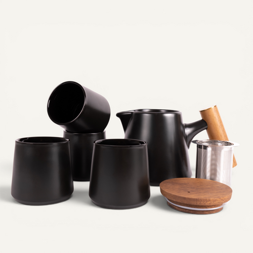 A set of black ceramic tea cups and a teapot with a solid walnut handle and a stainless steel infuser basket.