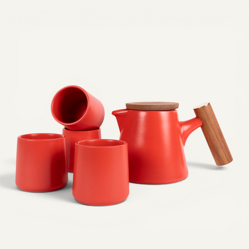 A set of red ceramic tea cups and a teapot with a solid walnut handle and a stainless steel infuser basket.